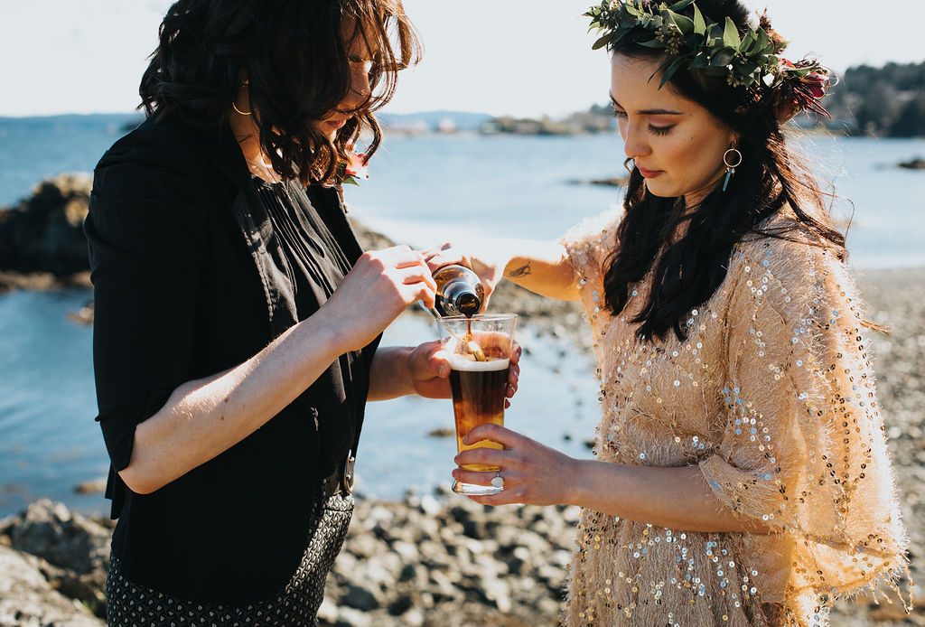 same sex couple pouring a black and tan in an elopement ceremony on the beach